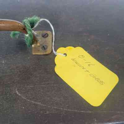 A rusty metal handle is attached to wood, with a yellow tag tied by string nearby.