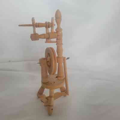 The image shows a miniature wooden spinning wheel with intricate details against a soft white background.
