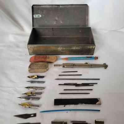 An open metal box with assorted vintage drawing tools, erasers, and pencils laid out neatly.