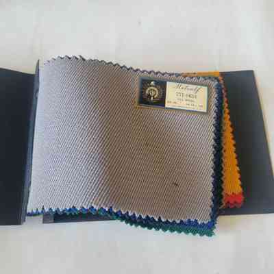 A fabric swatch book displays various textured textiles with a label identifying the material as all wool.