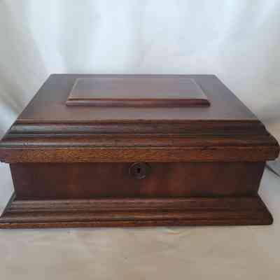 The image shows a closed, rectangular wooden box with a keyhole, against a soft white background.