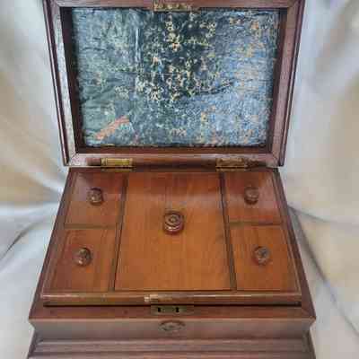 An open wooden box features multiple compartments and a worn, textured interior lid.