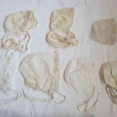 The image shows seven vintage white bonnets with various lace and ribbon details, displayed on a plain background