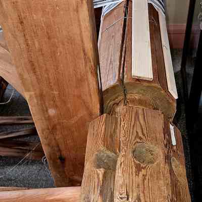 Warp beam.: The image showcases a traditional wooden loom, which is used for weaving textiles and features a large, sturdy warp beam made from rough-hewn wood, displaying natural grain patterns and some marks of wear, with several threads of light-colored yarn wound tightly around it, reflecting an element of handcrafted texture; the loom's wooden frame is visible in the background, indicating its intricate construction, and the setting—likely a museum—has a carpeted floor, suggesting an indoor environment that highlights the loom's historical and cultural significance, capturing the essence of traditional craftsmanship and the enduring legacy of handmade textile production.