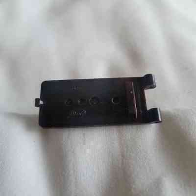 A small, dark brown plastic component with three holes is lying on a white fabric surface.