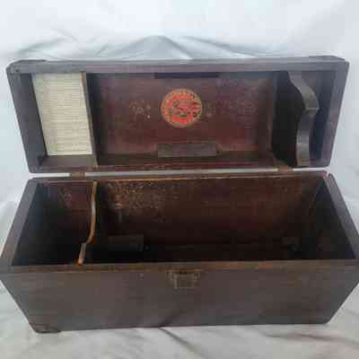 An open vintage wooden box with compartments and a visible paper label inside its lid, placed against a white background