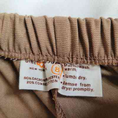 The image shows a garment label with washing instructions attached to brown elastic fabric.