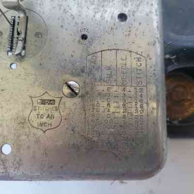 The image shows a metallic sewing machine plate with stitch settings chart