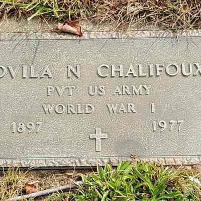 Grave of Ovila ["Ovid"] N. Chalifoux, St. Joseph Cemetery, Willimantic, CT.: The image shows a weathered, rectangular grave marker surrounded by grass, inscribed with "OVILA N CHALIFOUX" and denoting their rank as a private in the US Army during World War I, with the years of birth and death listed as 1897 and 1977, respectively; a small, engraved cross is present below the dates, symbolizing a Christian faith, and a rugged, textured border frames the plaque, suggesting its sturdy, durable design intended to withstand the elements and preserve the memory of the deceased individual for posterity, amidst the serene, natural surroundings of