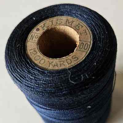 Photo of Spool of Thread: A photograph of a spool or tube of blue cotton thread, viewed from the bottom so as to show the label. The spool is shown to be made of wood.
