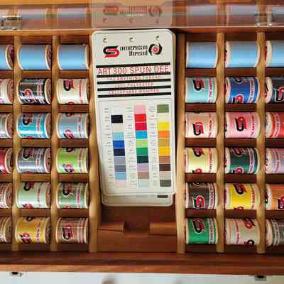 The inside of the case, featuring eighteen spools of different colored thread on each side of a collection of sample cards featuring the American Thread Co and Spun Dee logos.