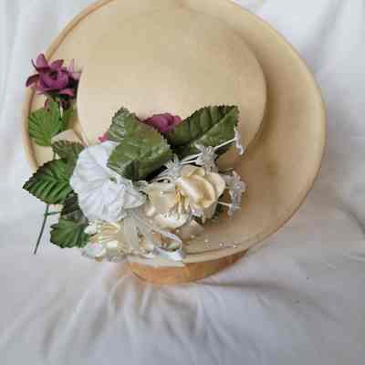 A beige hat adorned with green leaves and beautiful, colorful flowers rests elegantly on a plain background.