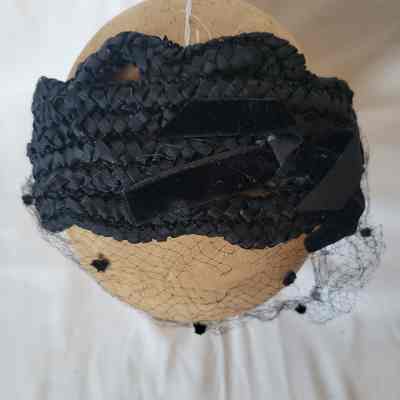 A black vintage hat adorned with netting and small velvet accents sits atop a beige mannequin head.