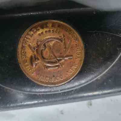 The image shows a round, metallic emblem labeled “Wilcox & Gibbs,” affixed to a dark surface