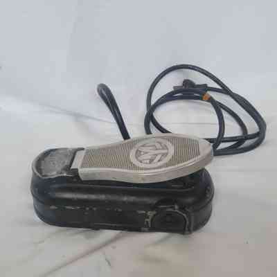 A worn black foot pedal with cable lies on a white surface.