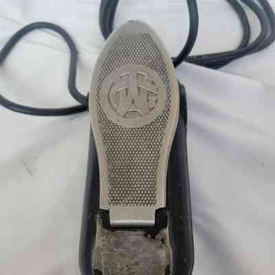 The image shows a metallic foot pedal with a textured surface and an engraved emblem.