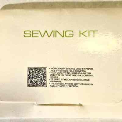 Sewing kit, closed. Back.: A white cardboard square. It structure of the kit holder is revealed to be a piece of cardboard folded in half, with a tab that inserts into a slot to keep it closed. Contains the words "sewing kit," a QR code, and small print identifying where the cardboard was manufactured and printed.