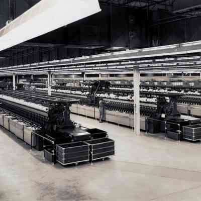 Winding room: A worker stands in a large room filled with what appear to be thread winding machines in 1966. The absence of overhead drive shafts indicates that the machines are probably  powered by electric motors.