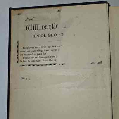 Bookplate: The image shows an open book with a partially visible page attached inside the front cover, featuring text about a library policy from the "Willimantic Spool Shop." It indicates that employees may take out one volume at a time for a period not exceeding three weeks, with lost or damaged books requiring compensation before further borrowing is allowed. The paper appears old and is affixed to the page, showing signs of wear and faded text, with some handwritten numbers, "N012," near the bottom left corner, adding a historical and personal touch to the document.