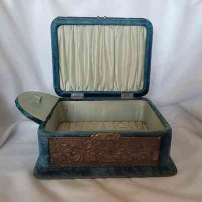 The open vintage jewelry box is lined with pale fabric and has ornate floral detailing outside.