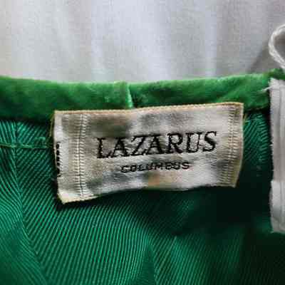 The image shows a clothing tag labeled "Lazarus Columbus" sewn onto green fabric.