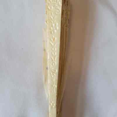 The image shows the side of the closed fan with carved intricate floral patterns on a white background.