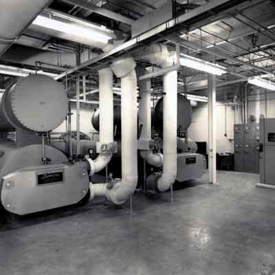 Large room with unknown machines: A large room holds large machines connected to large pipes. Possibly this is a steam plant.