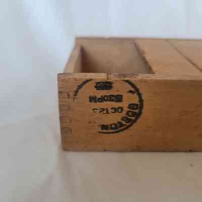 The image shows a wooden box with a circular stamp marking on its side, partially visible.