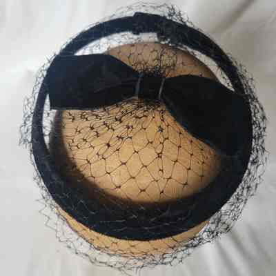 A black headband with a bow and net veil rests on a mannequin head.