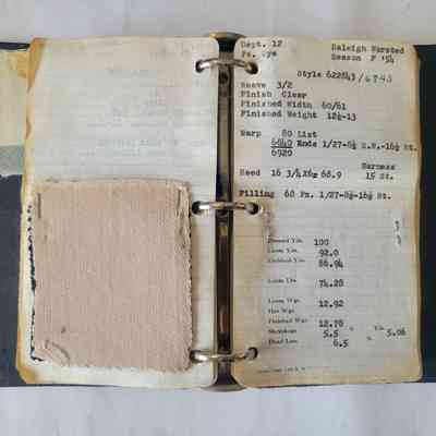 An open binder displays fabric samples, notes, and specifications related to textile production and measurements.