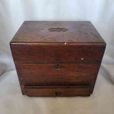 A rustic wooden box with a keyhole sits on a white fabric background, showing signs of age.