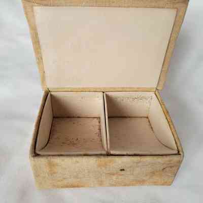 The image shows an open, vintage jewelry box with two compartments, displaying signs of age and wear.