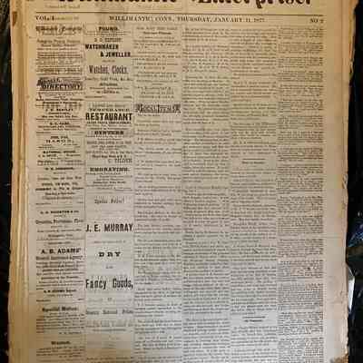 Willimantic Enterprise January 11th 1877: This is the cover page of the Willimantic Enterprise Vol. 1 No. 2 dated January 11th, 1877. There are six columns of text across. The first two columns are primarily comprised of advertisements. The following columns contain news articles. On the left side of the page, some of the print from the previous page has been transferred onto this sheet of paper. The paper is yellowed and the edges are frayed from age.