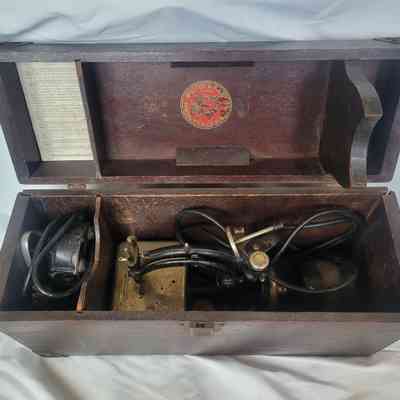 The image shows an antique wooden box opened, revealing intricate electrical equipment inside.