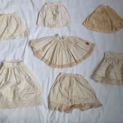The image shows seven vintage doll skirts with lace details, arranged on white fabric.