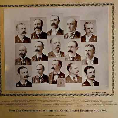 Photo with matte: This image features a sepia-toned historical photograph of the first city government of Willimantic, Connecticut, elected on December 4, 1893. There are 15 individual portraits arranged in three rows, each showcasing men with distinguished mustaches, indicative of the fashion of the time. The central figure is identified as Mayor George M. Harrington. Each portrait is numbered, and the names corresponding to each number are listed below the photos, along with their roles, such as aldermen and councilmen. The photograph is bordered with an ornate floral pattern, adding to its vintage aesthetic.