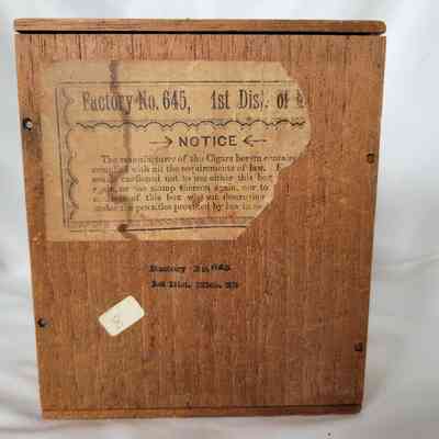 The image depicts a wooden box with an old, partially torn label describing factory and cigar information.