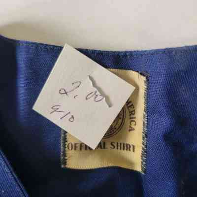 A blue shirt has an attached price tag and a visible manufacturer’s label underneath.