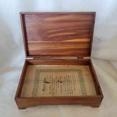 The wooden box with an open lid contains a certification paper on its base.