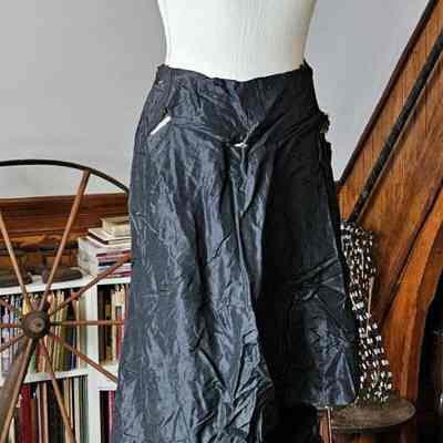 Front of the skirt.: A long, black, floor-length, silk skirt hangs from a mannequin. The photo is taken from the front. Several holes in the silk are visible. Ruffles decorate the hem.