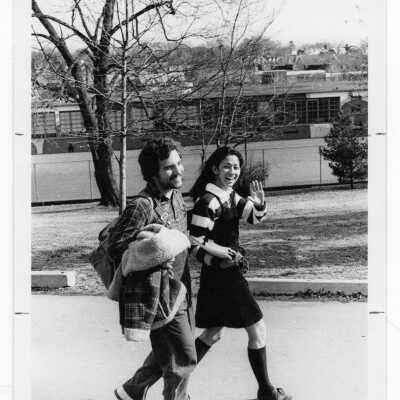 Two students walking with elementary school in background.
