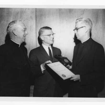 Mark Bauer, S.J., showing Shaffrey award certificate and award to J. Joseph Bluett, S.J. and Dr. Hilferty, president of medical alumn, 1961.