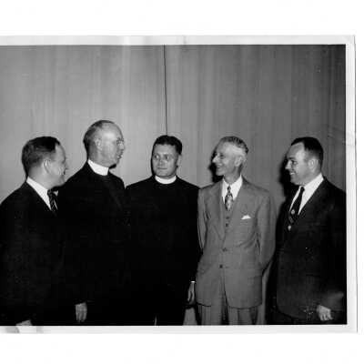 Dennis J. Comey, S.J., Edward G. Jacklin, S.J, Daniel Dougherty (?), and others conferring during alumni communion breakfast, October 26, 1952.