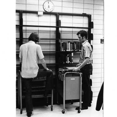 Interior view two students in Drexel Library sorting books for reshelving.