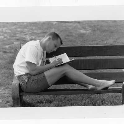Student wearing shorts reading on park bench.