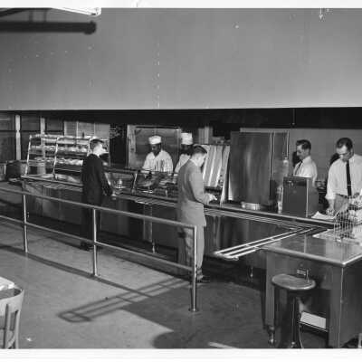 Interior view of two students in cafeteria line with food service employees.