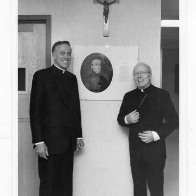 Donald I. MacLean, S.J. standing next to photograph of Edward J. Sourin, S.J. at dedication of Sourin Residence Center.