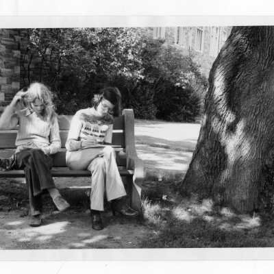 Two women students sitting on park bench, studying, near Barbelin building.