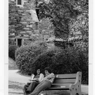 Two students sitting on park bench near Barbelin building.