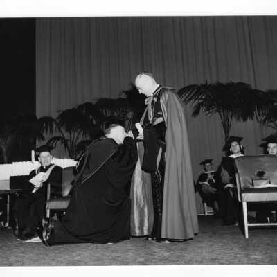 Edward G. Jacklin, S.J., kissing ring of Bishop John J. O'Hara during 1954 graduation/commencement ceremony.